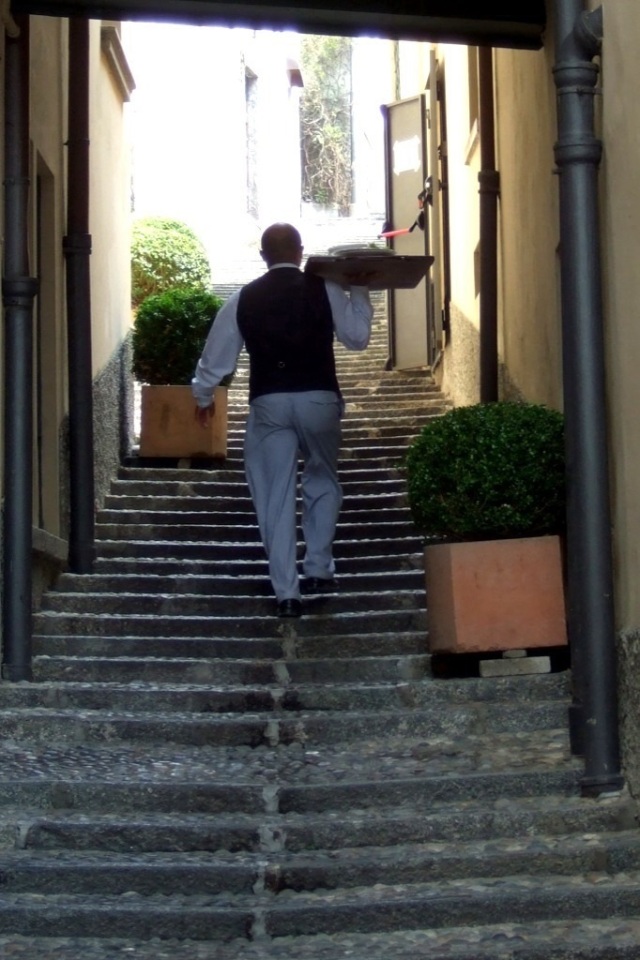 Waiter carrying a tray up a staircase in Bellagio, Italy